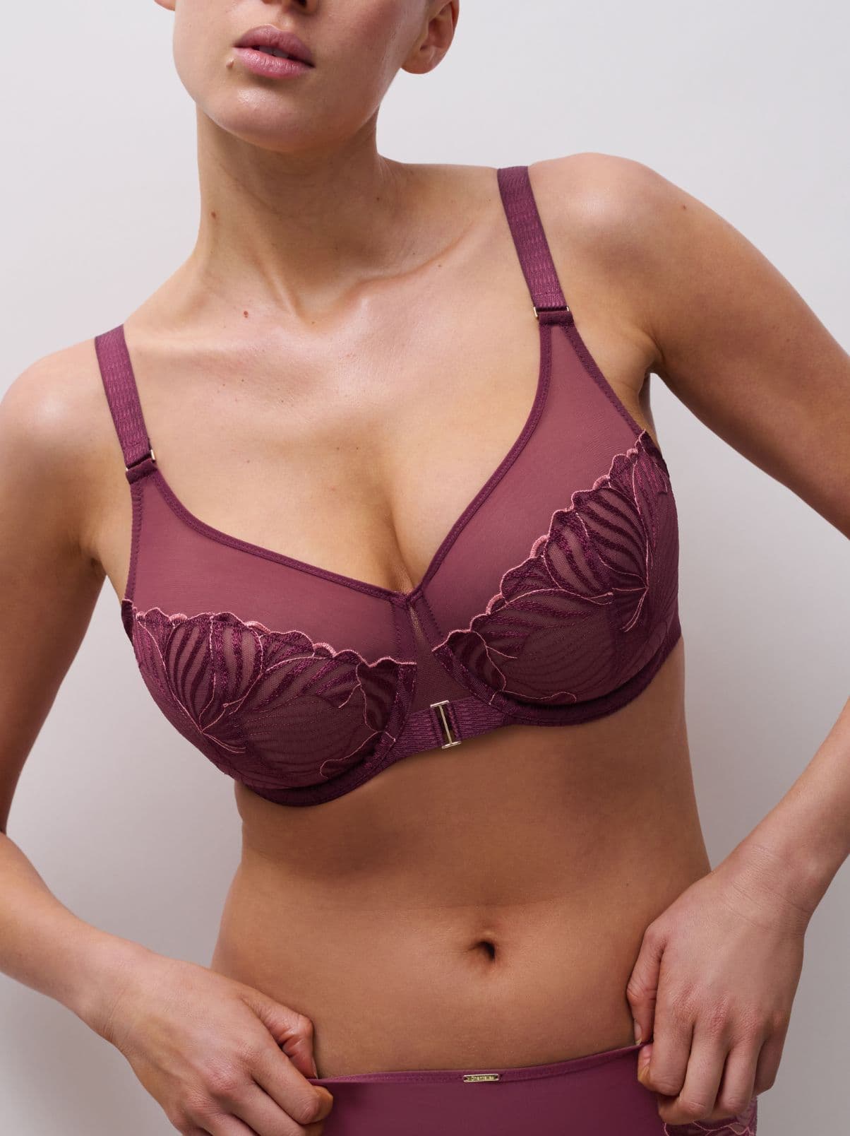 Person wearing a burgundy lace bra with floral embroidery, posing against a plain background.