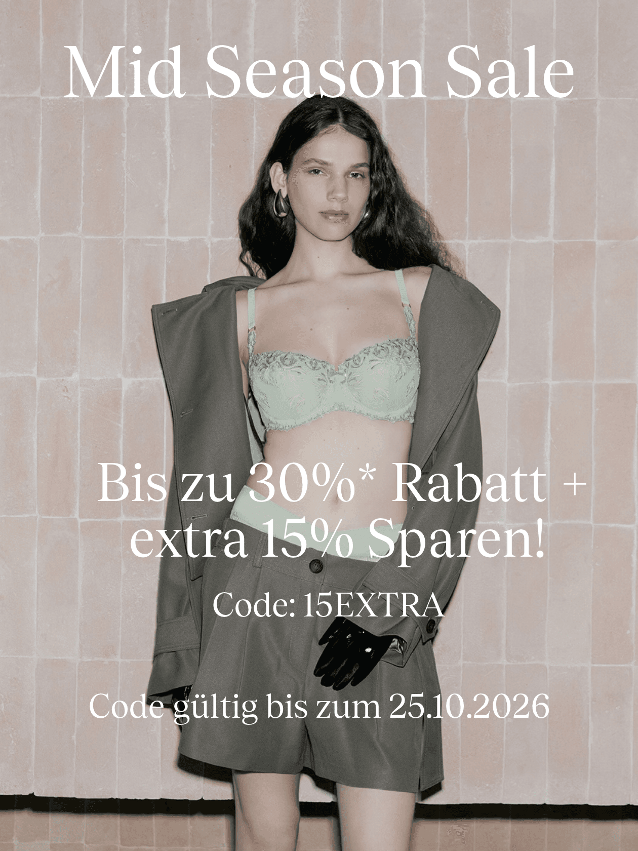 Woman in a green lace bra and brown suit poses against a tiled wall. Text: "Mid Season Sale" with discount details and code "15EXTRA". Valid until 25.10.2026.