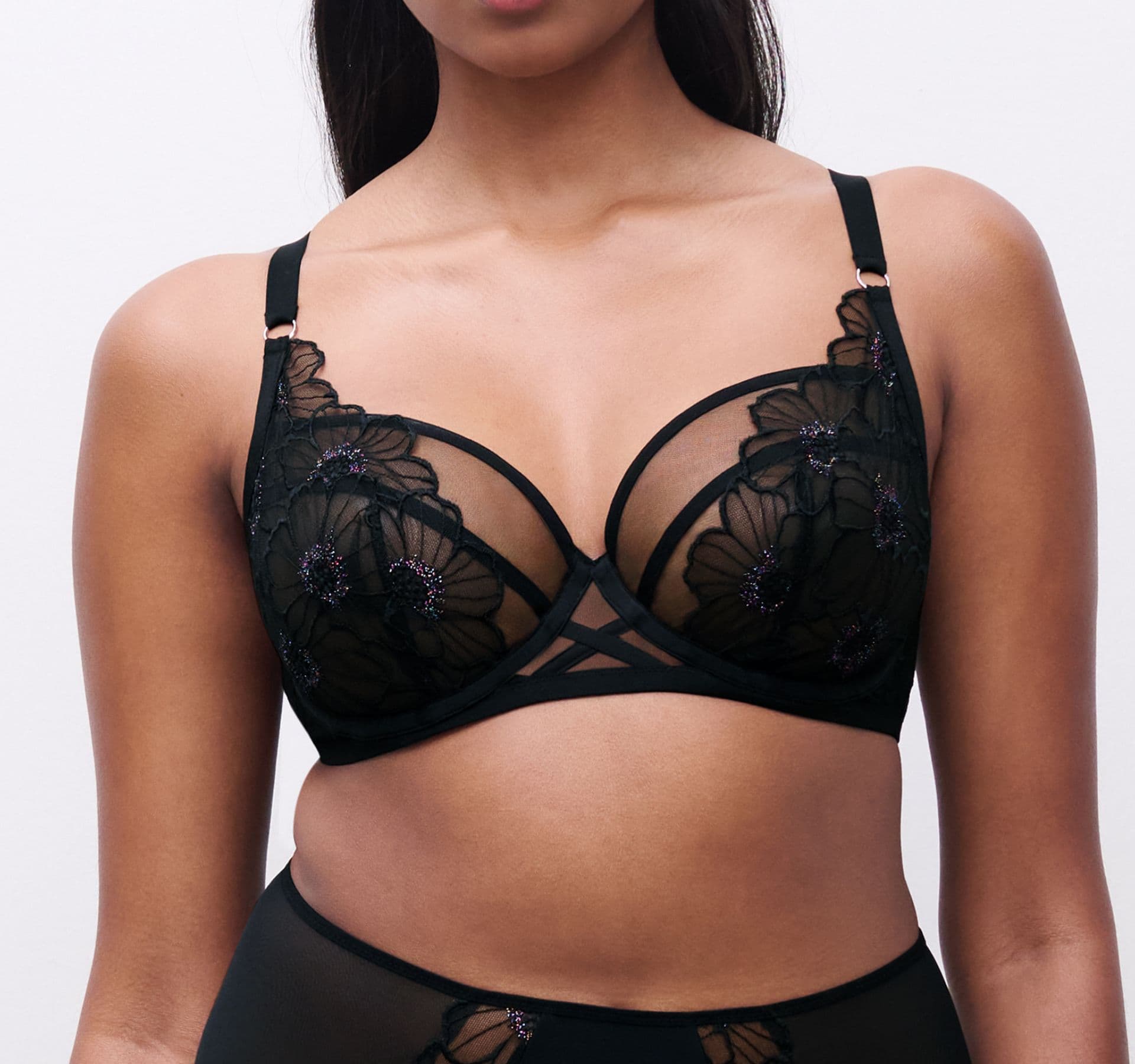 Person wearing a black lace bra with floral embroidery and a matching bottom, standing against a plain white background.