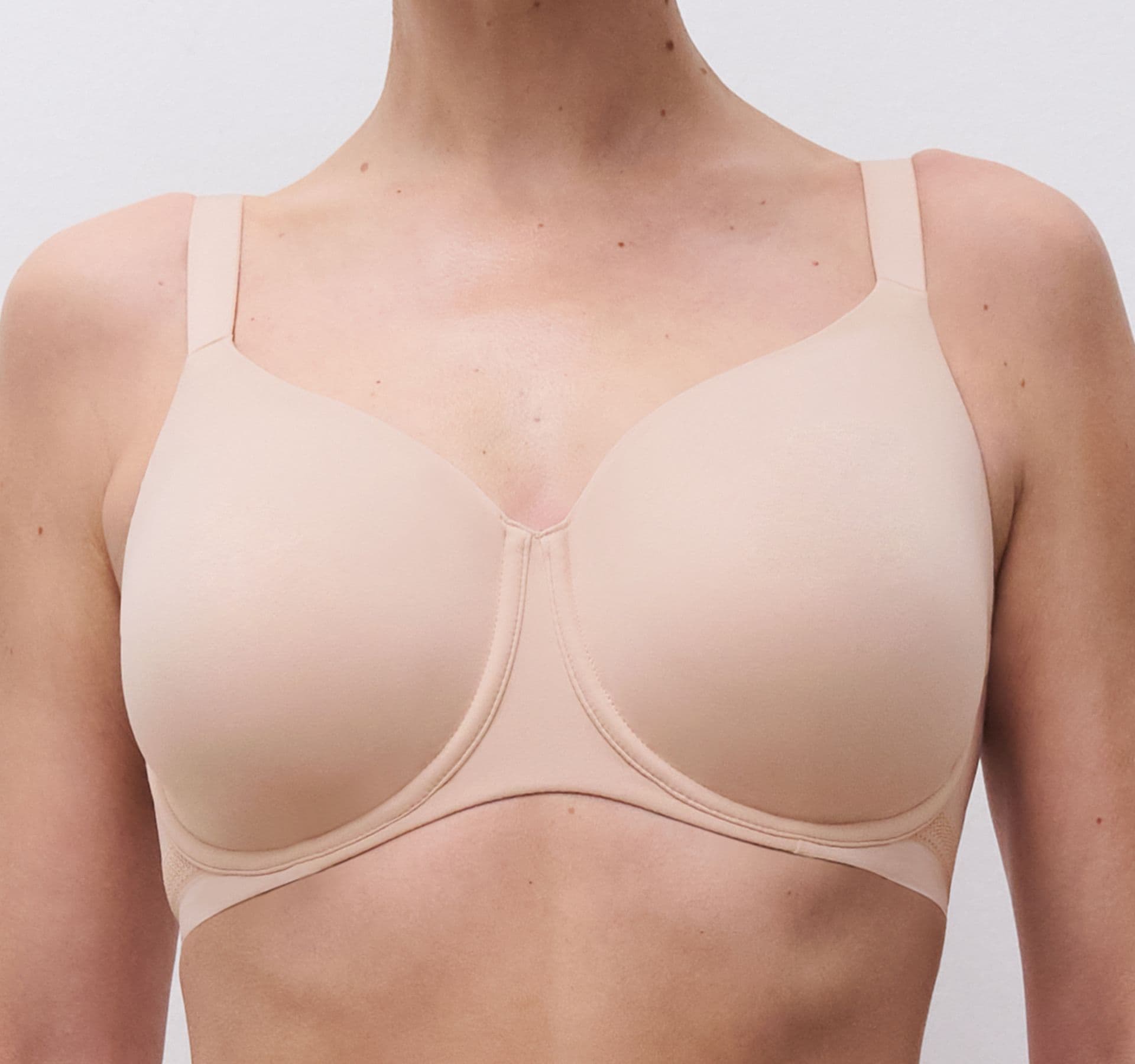 A person wearing a beige bra with wide straps and smooth cups, standing against a plain white background.