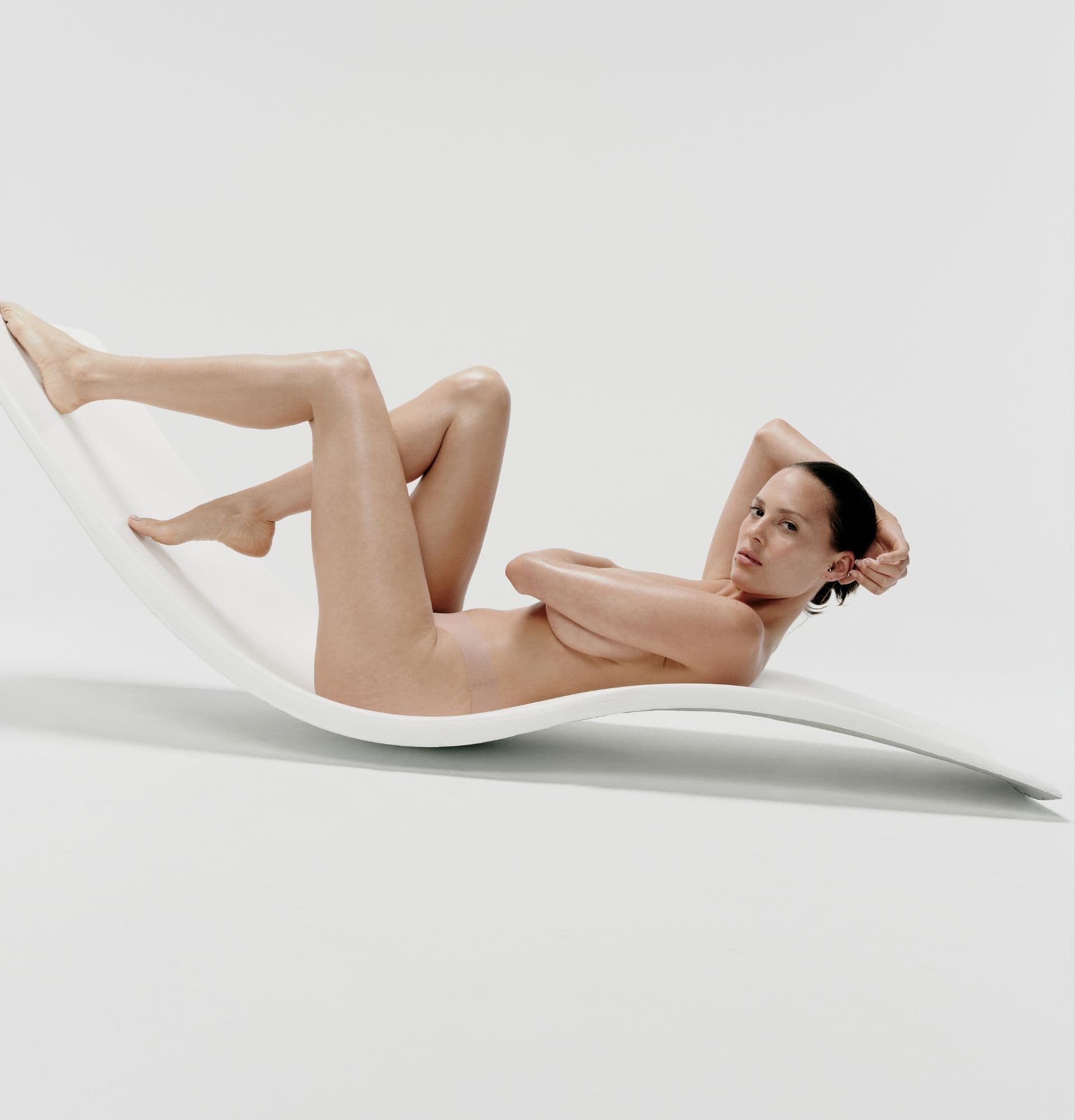 Person reclining on a modern, curved white lounge chair against a plain white background, striking a relaxed pose.