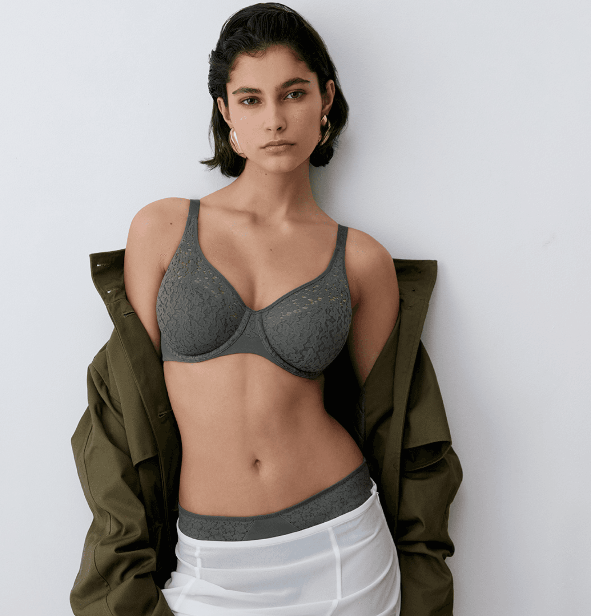 Woman wearing a lace lingerie set and an open jacket, standing against a white background.