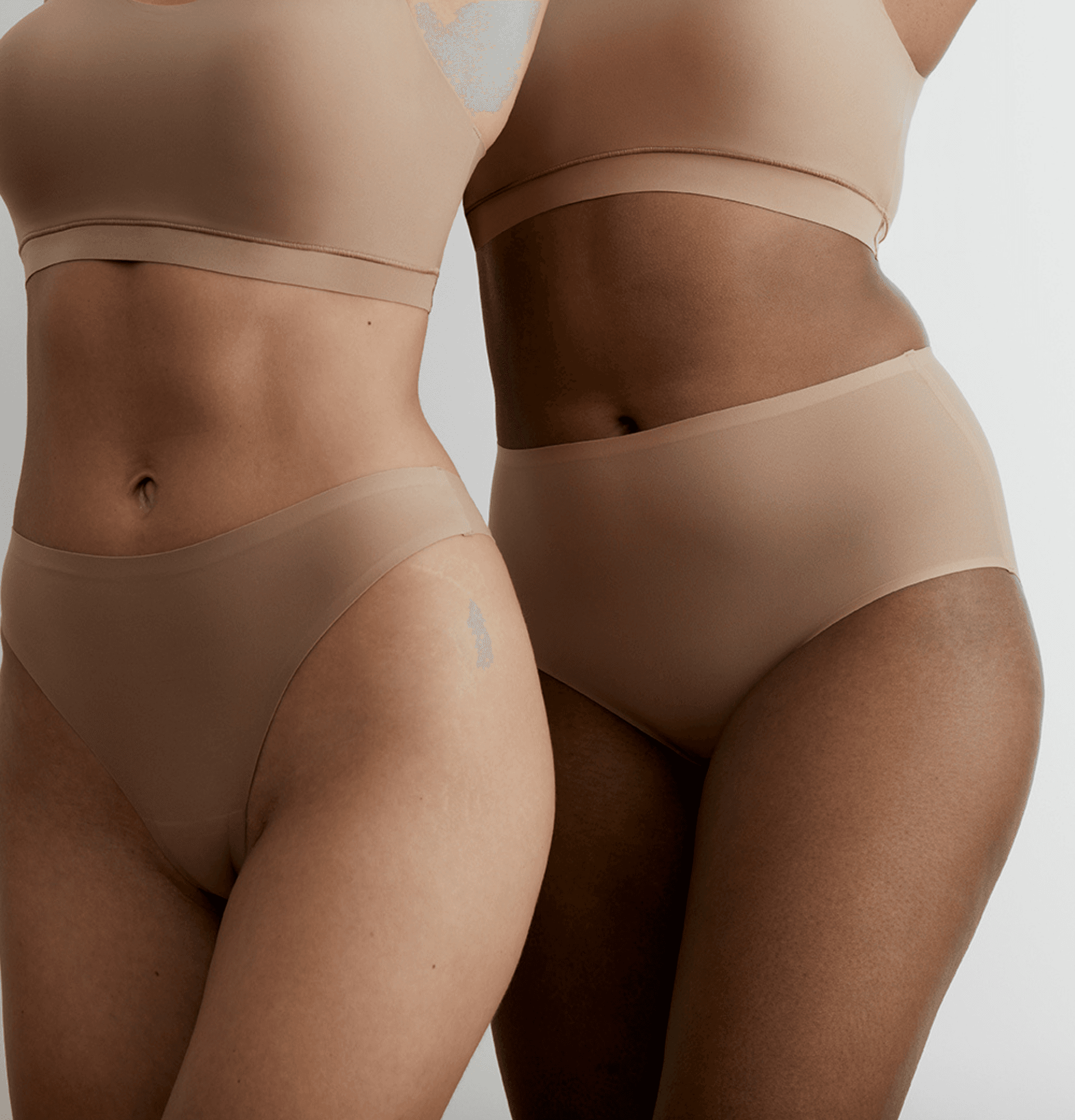 Two women wearing seamless, nude-toned underwear; close-up of midsections with hands relaxed at sides.