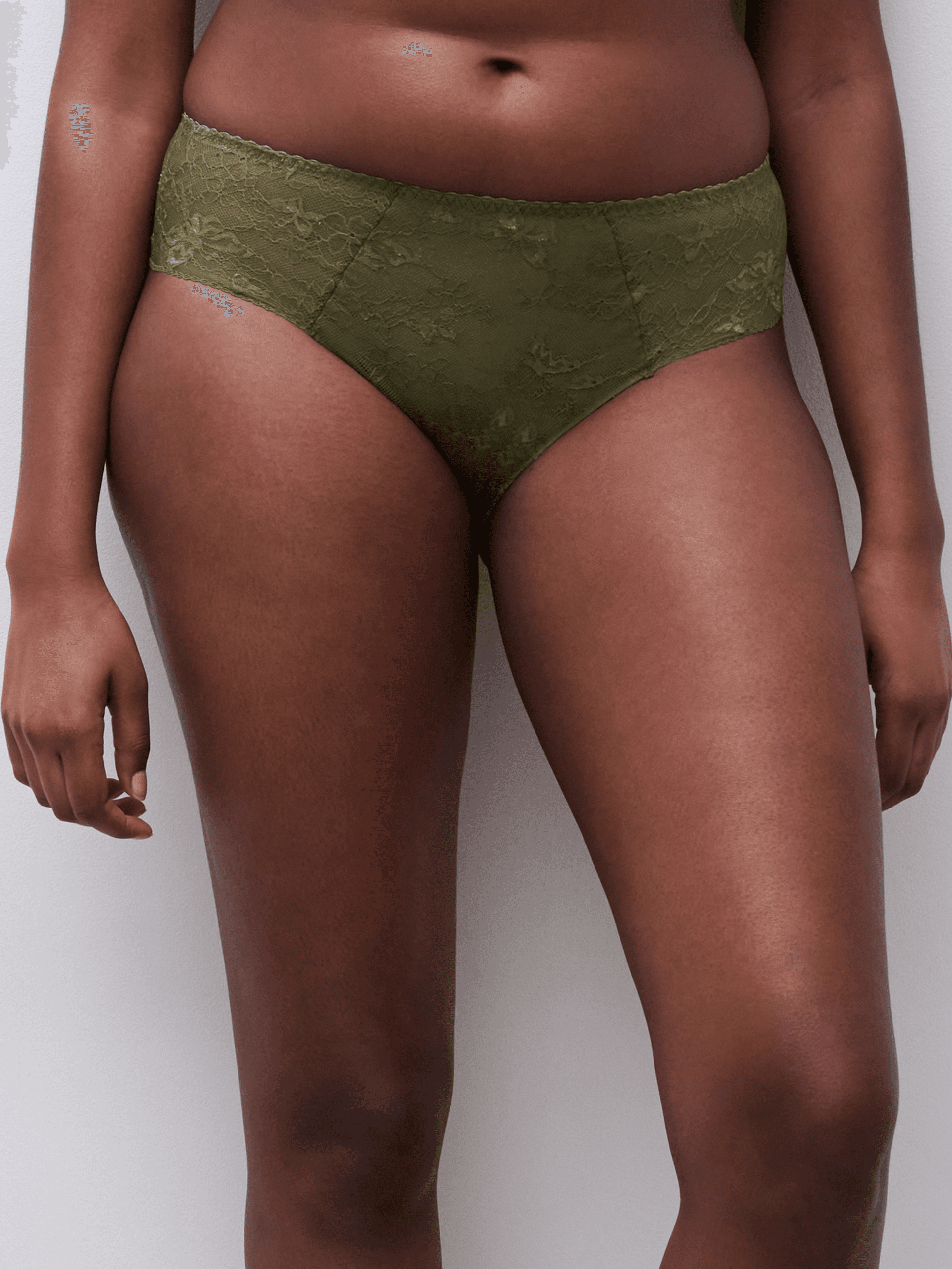 A person wearing olive green lace high-waisted underwear stands against a neutral background.