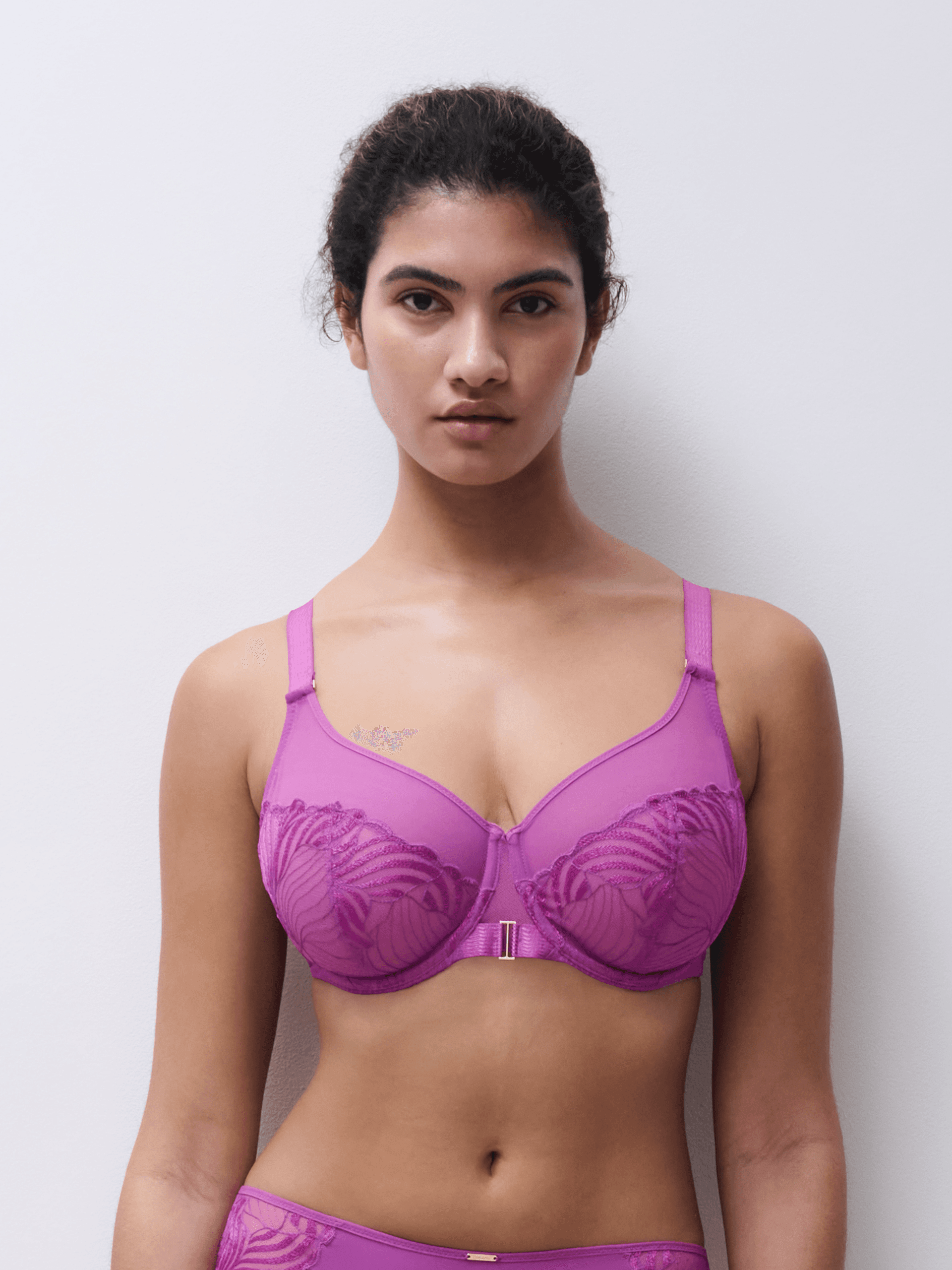 A person is wearing a purple lace-design bra and matching bottoms, standing against a plain white background.