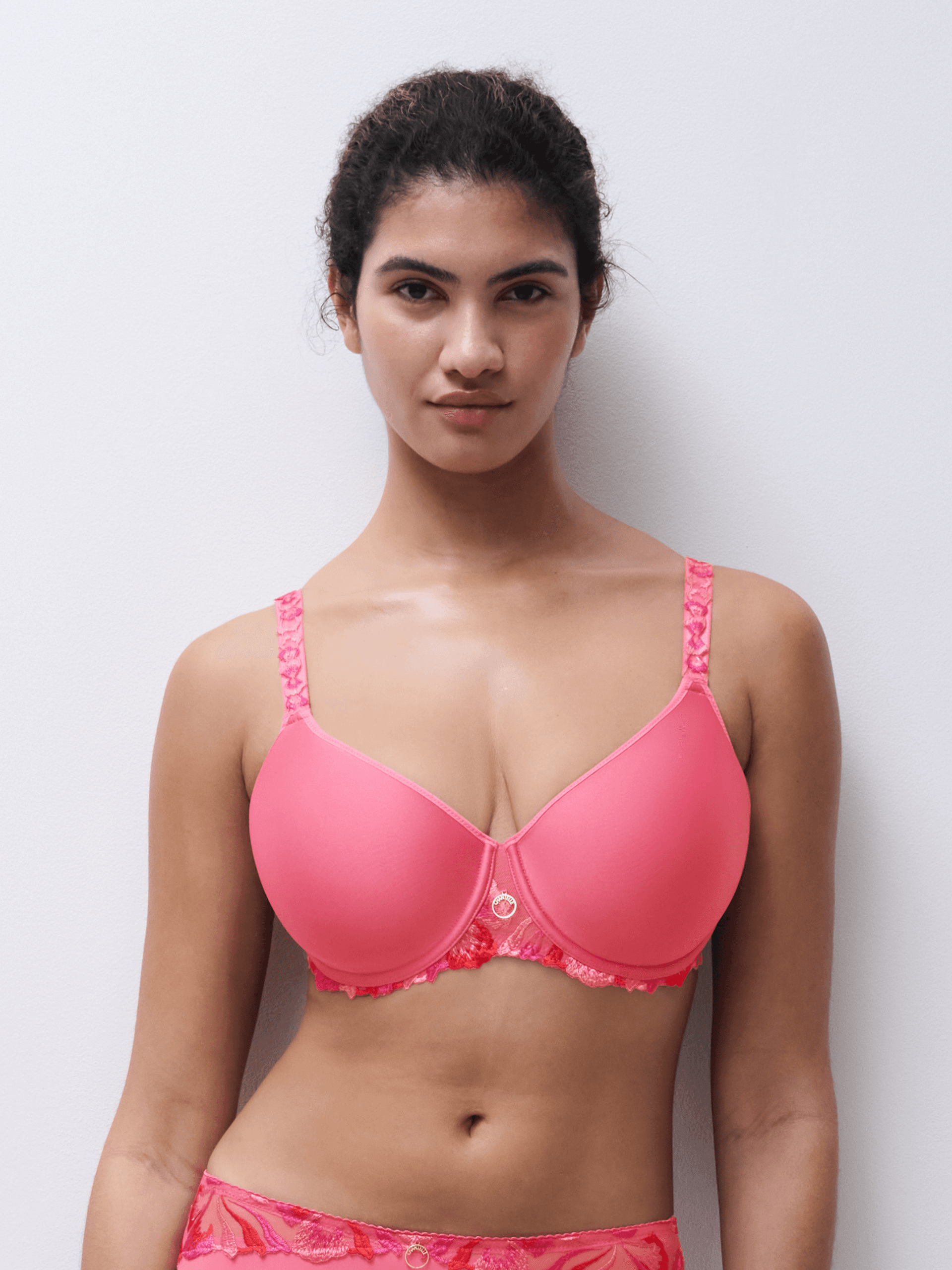 Person wearing a vibrant pink bra with lace details, standing against a light gray background.