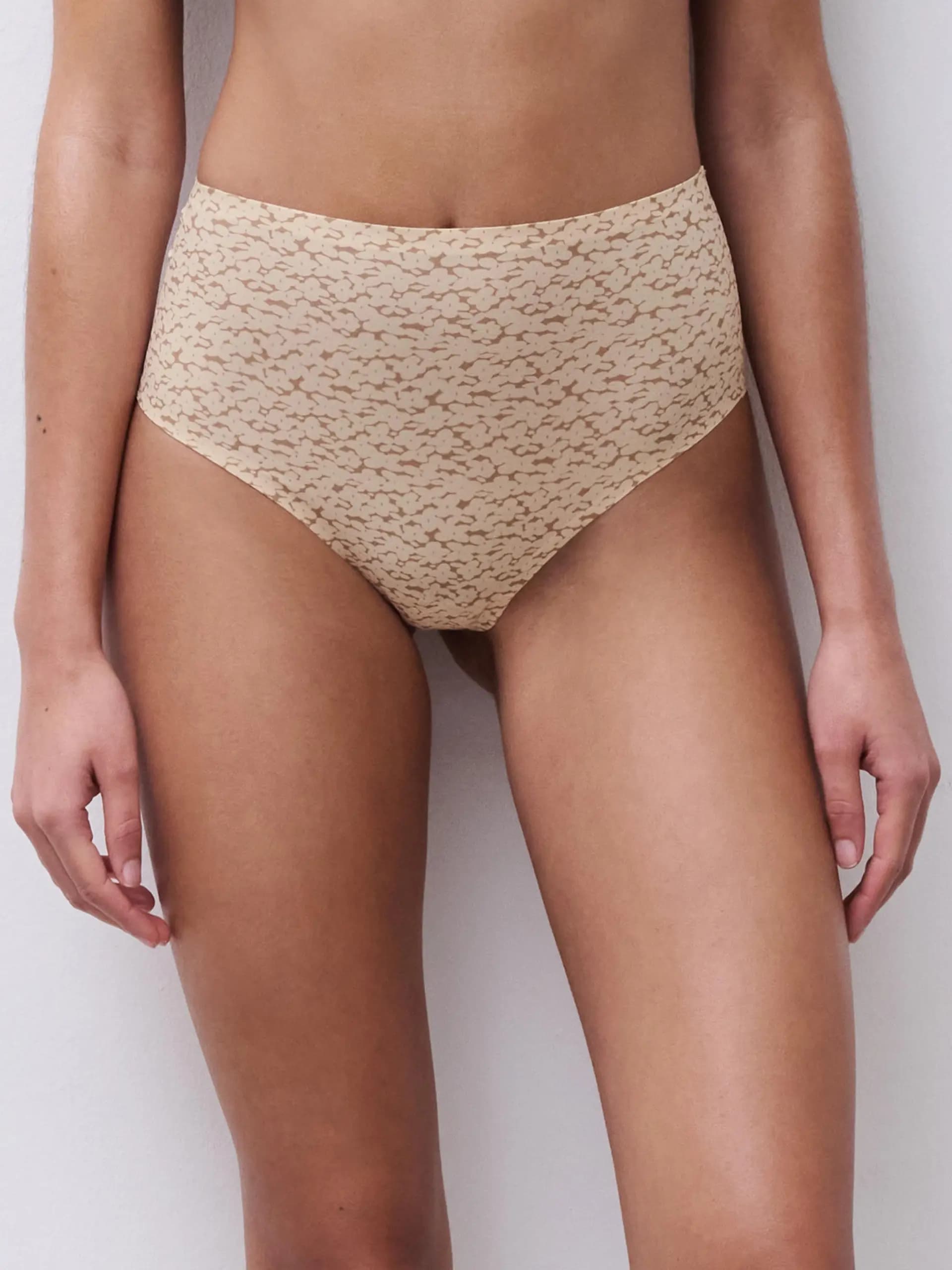 Model wearing high-waisted, patterned beige lingerie with a seamless design, standing against a light background.