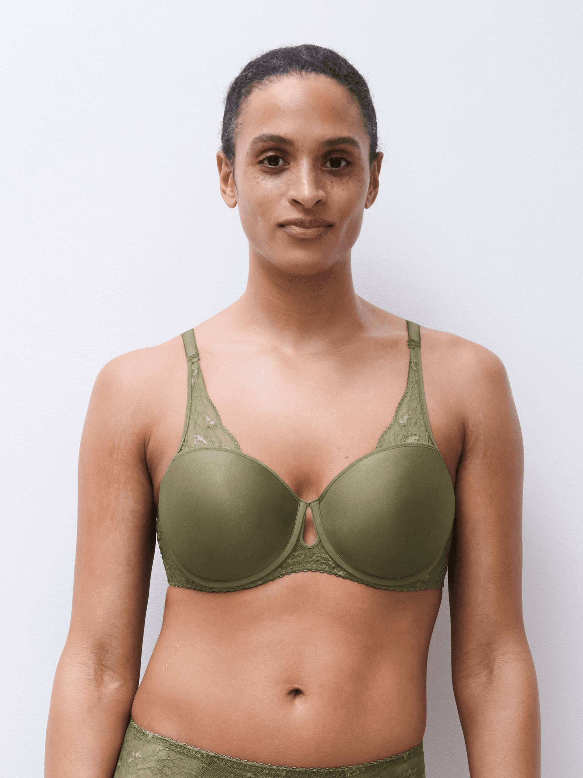 A woman wearing an olive green underwear set stands against a plain white background, looking directly at the camera.