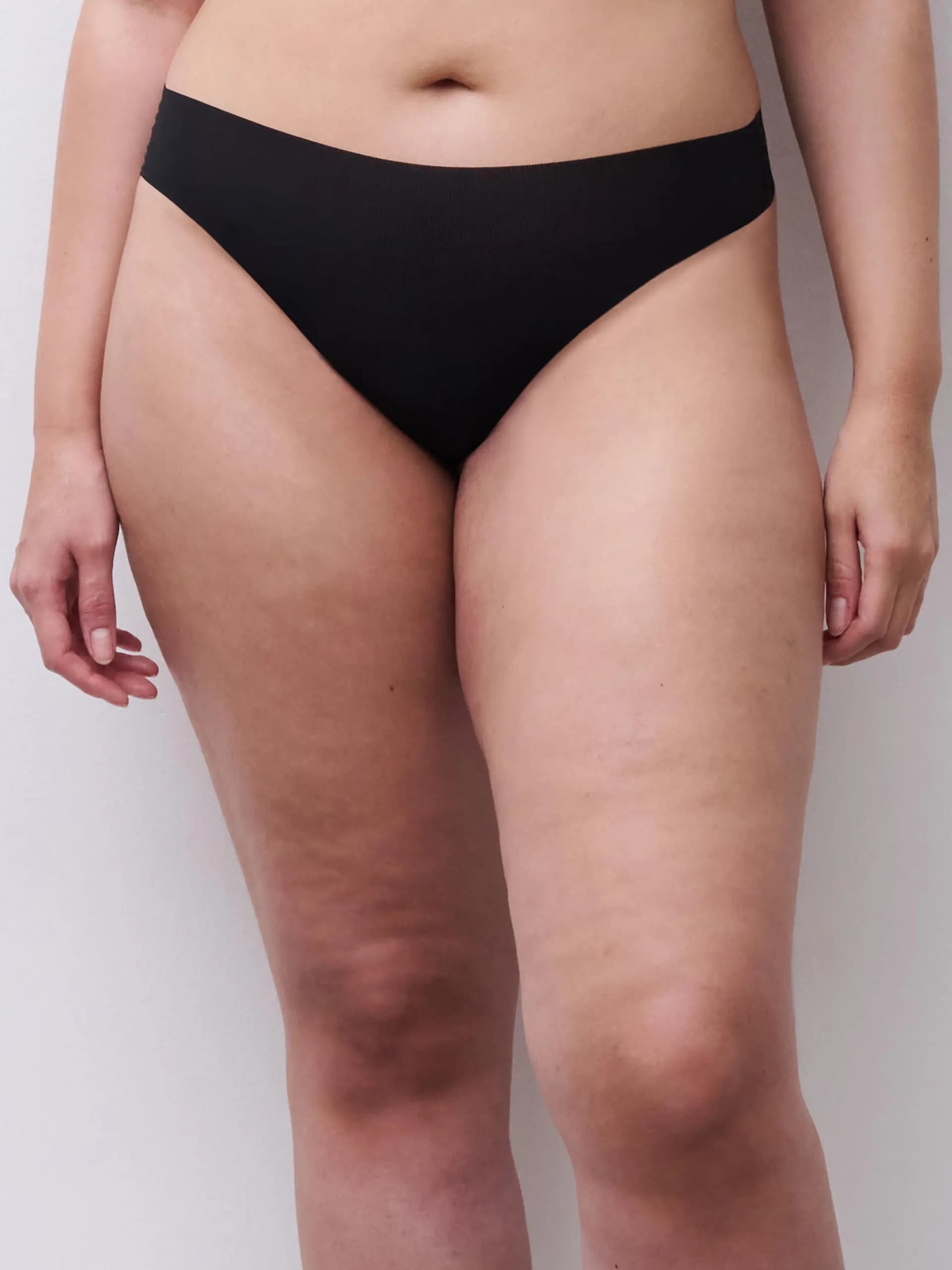 Person in black underwear against a light background, showcasing the natural texture of the skin on the legs and midsection.