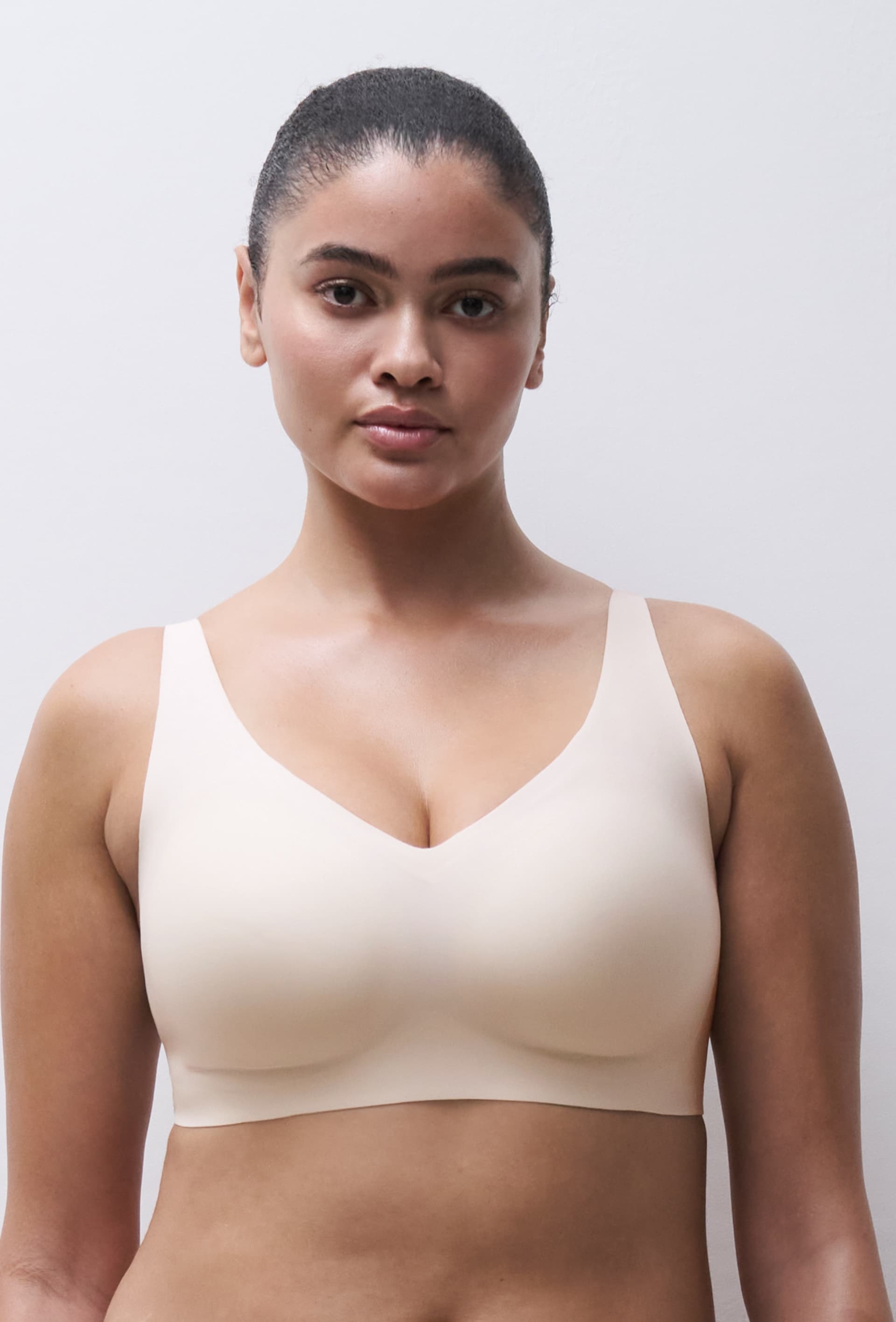 Woman in a beige, seamless bra stands against a neutral background, looking confidently at the camera.