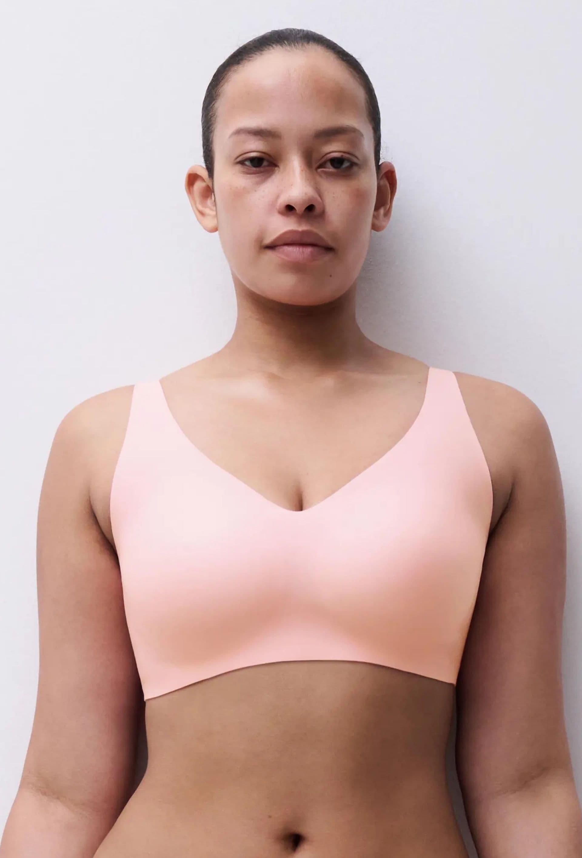 Person wearing a light pink, seamless bra, standing against a plain white background.