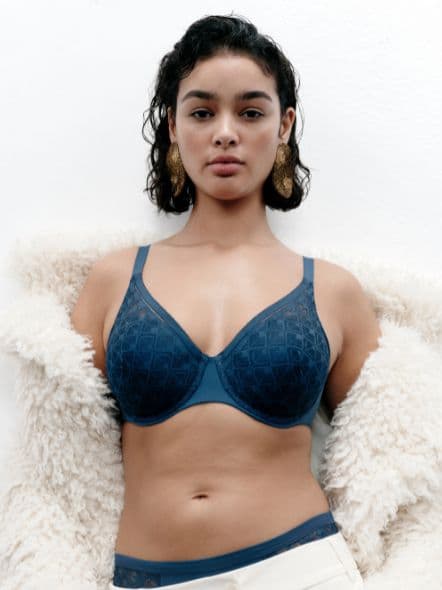 Person wearing a blue bra and cream coat, standing against a white background.