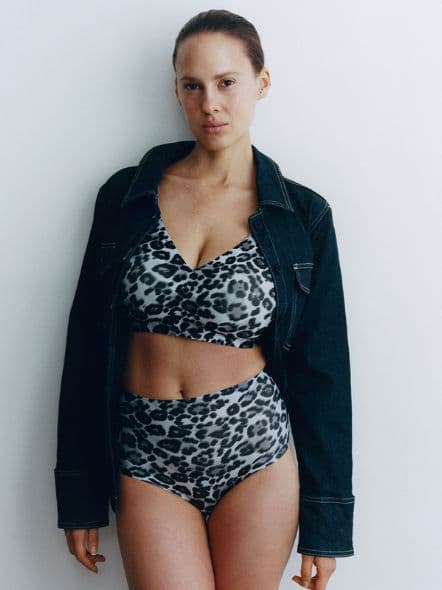 Person wearing a leopard print bikini and a dark denim jacket, standing against a plain white background.