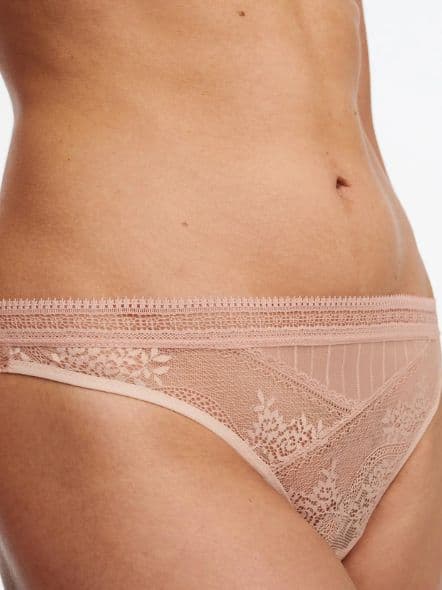 Close-up of a person wearing light pink lace underwear, showing intricate floral patterns and a decorative waistband.