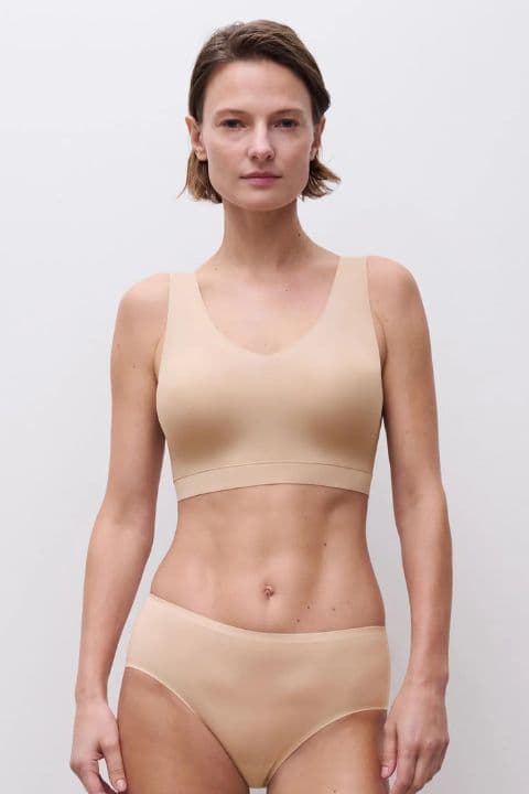 A person wearing a nude-colored seamless bra and underwear set stands against a plain white background.