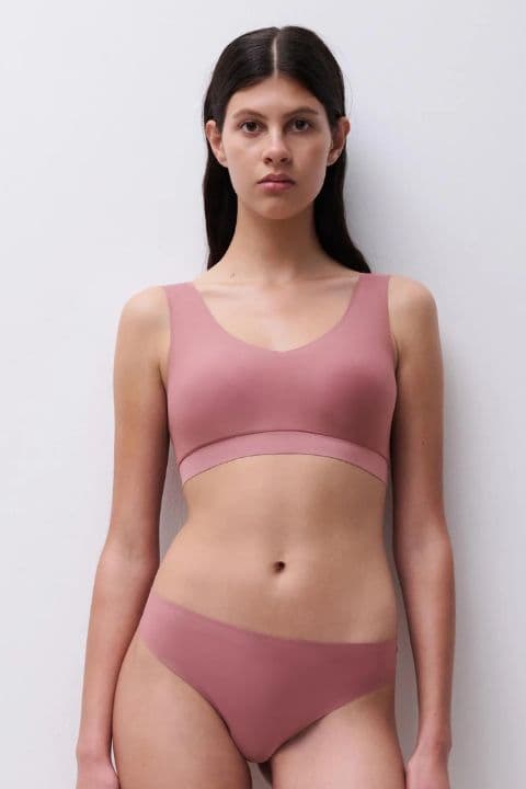 A person wearing a pink, seamless two-piece undergarment set stands against a plain white background.