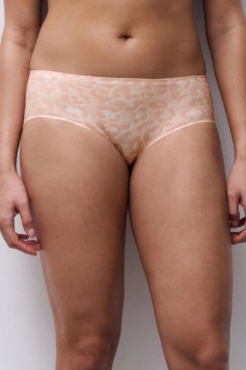 A person wearing soft pink, seamless underwear with a subtle animal print pattern, standing against a plain background.