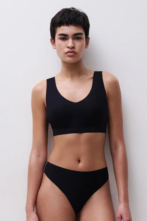 Person wearing a black bra and  underwear, standing against a plain white background.