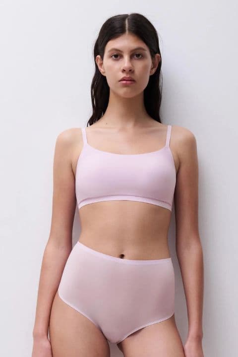 Woman in light mauve colored bra and high-waisted underwear poses against a plain white background.