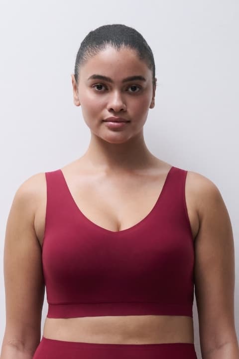 Woman in a red bra stands against a plain white background, looking directly at the camera.
