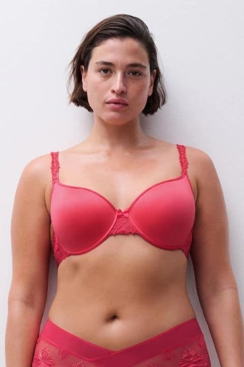 A person wearing a red bra with lace detailing, standing against a plain white background.