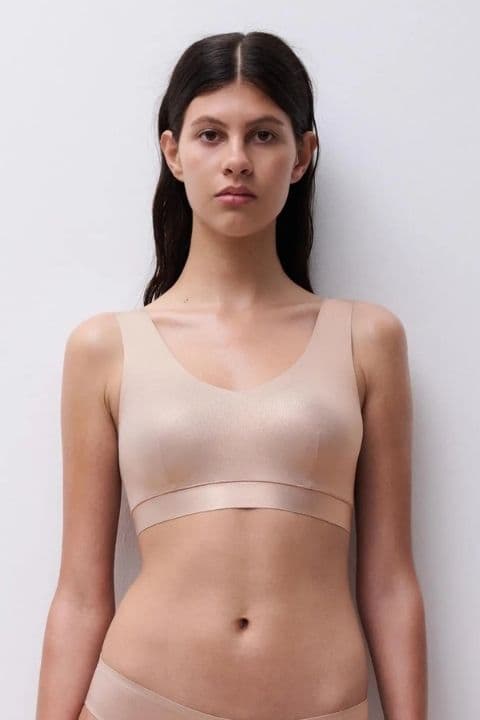 Person with long dark hair wearing a beige sports bra, standing against a plain white background.