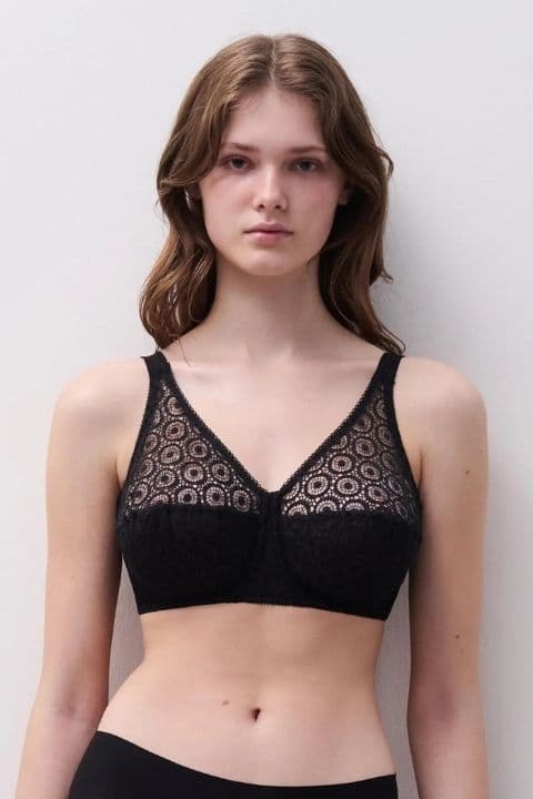 Woman wearing a black lace bra with a circular pattern, standing against a plain white background.