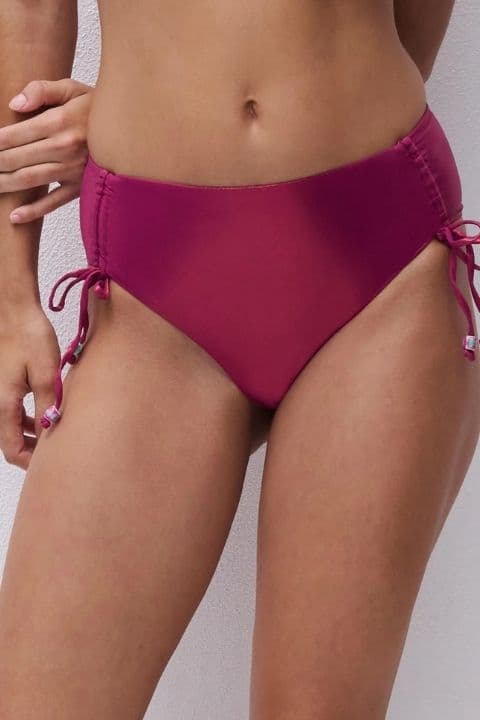Person wearing high-waisted magenta bikini bottoms with side ties, standing against a white background.