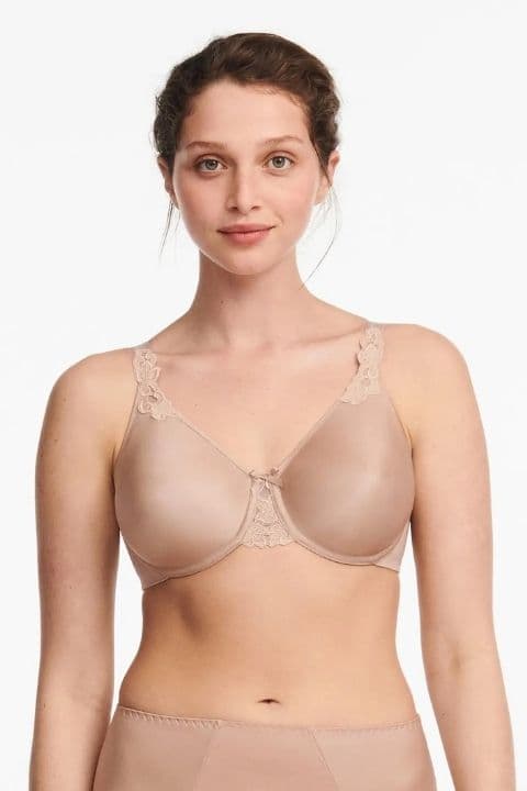 A woman wearing a beige bra with lace detail stands against a white background.