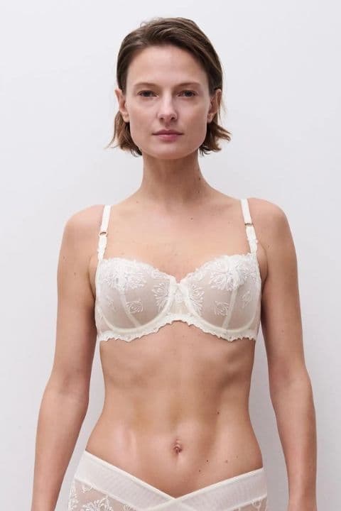 Person wearing a white lace bra and matching underwear, standing against a plain white background.