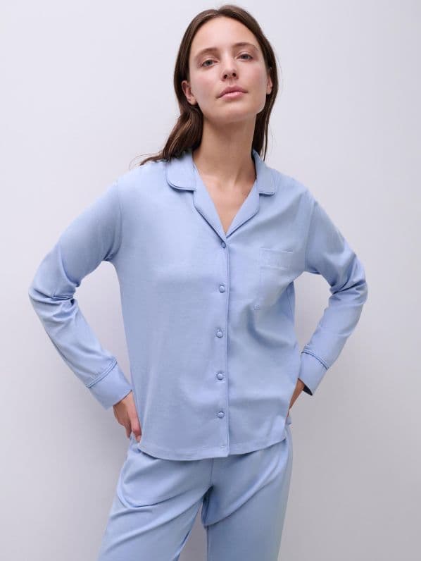Person wearing light blue pajamas with a button-up top and pants, standing against a plain white background.
