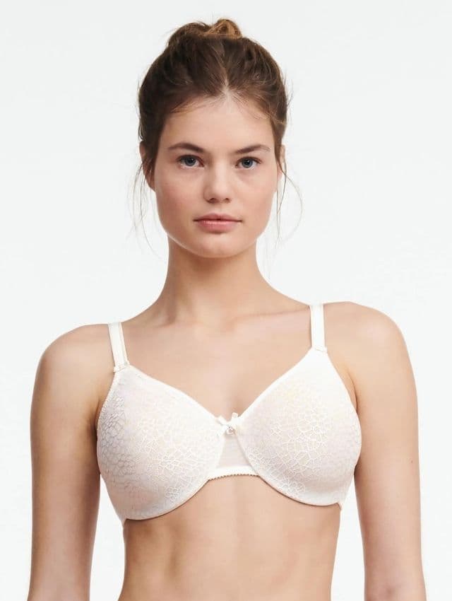 Woman wearing a lace-patterned white bra with thin straps, standing against a plain background.