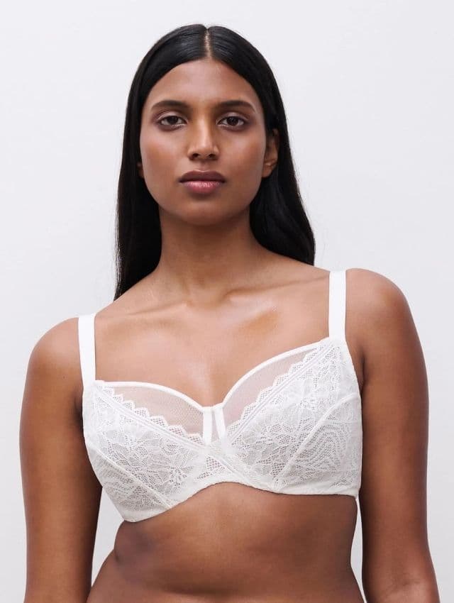 A person wearing a white lace bra with thin straps, against a plain background.
