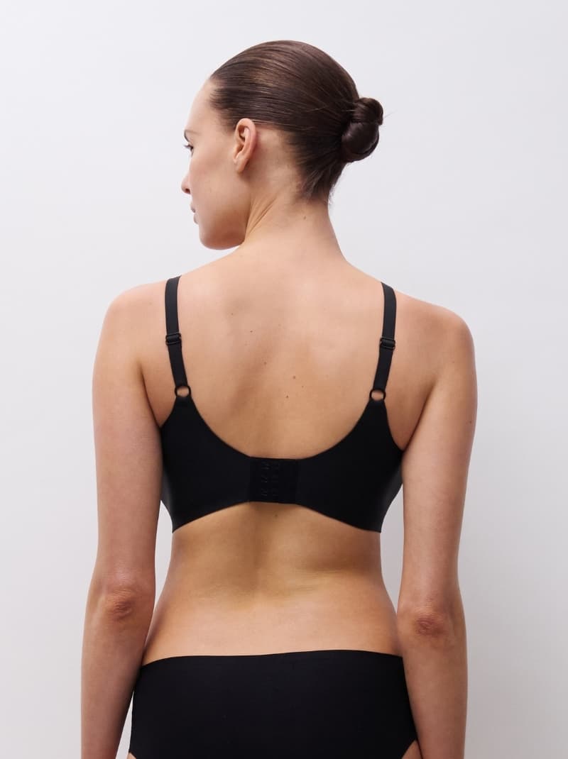 Person with a bun hairstyle wearing a black bra and panties, shown from the back against a plain background.