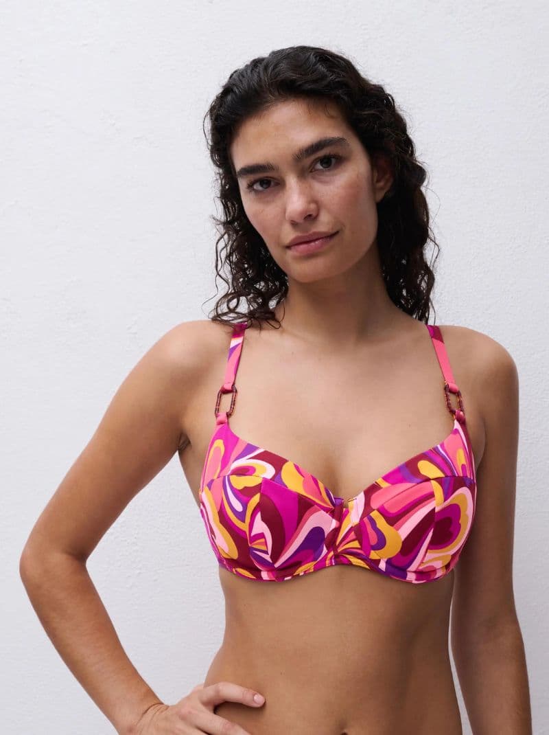 Woman in a colorful patterned bikini top with pink, yellow, and purple designs, standing against a plain white background.