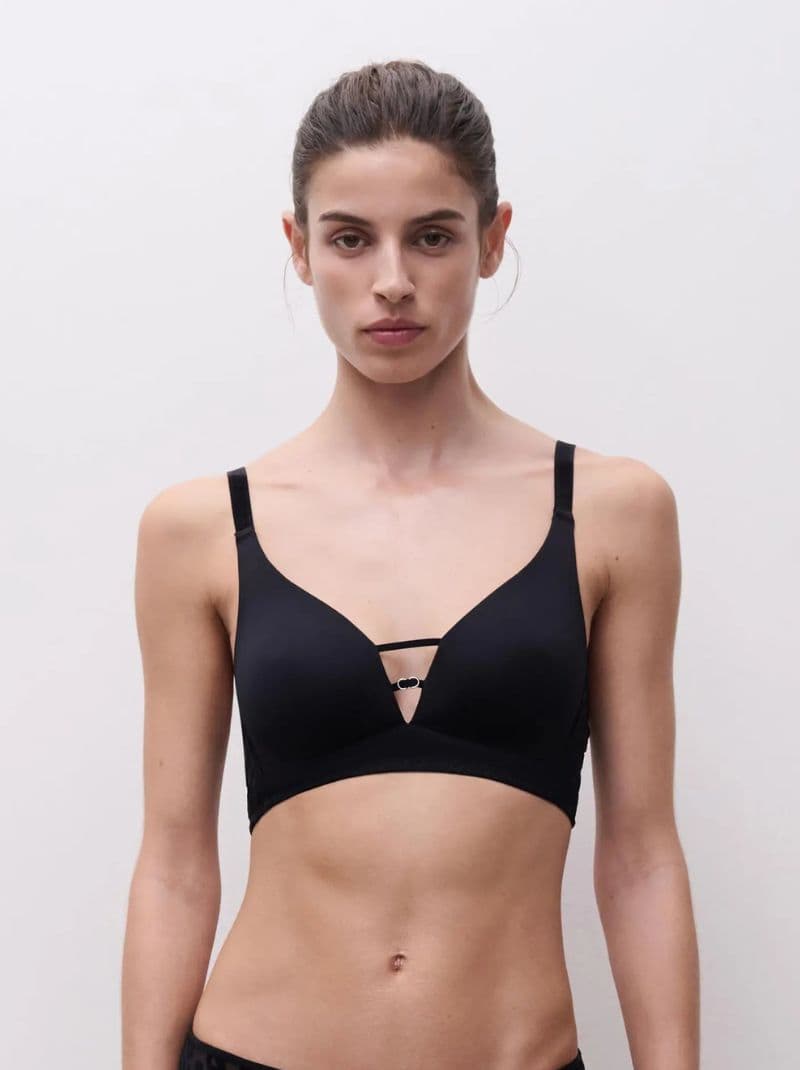 Person wearing a black bra with thin straps and a simple design against a plain background.