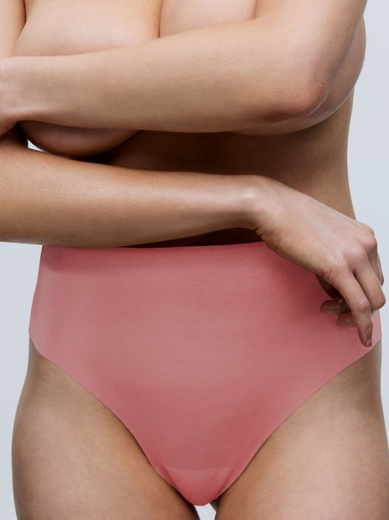 Person wearing high-waisted guave colored underwear, arms crossed over chest, shown against a neutral background.