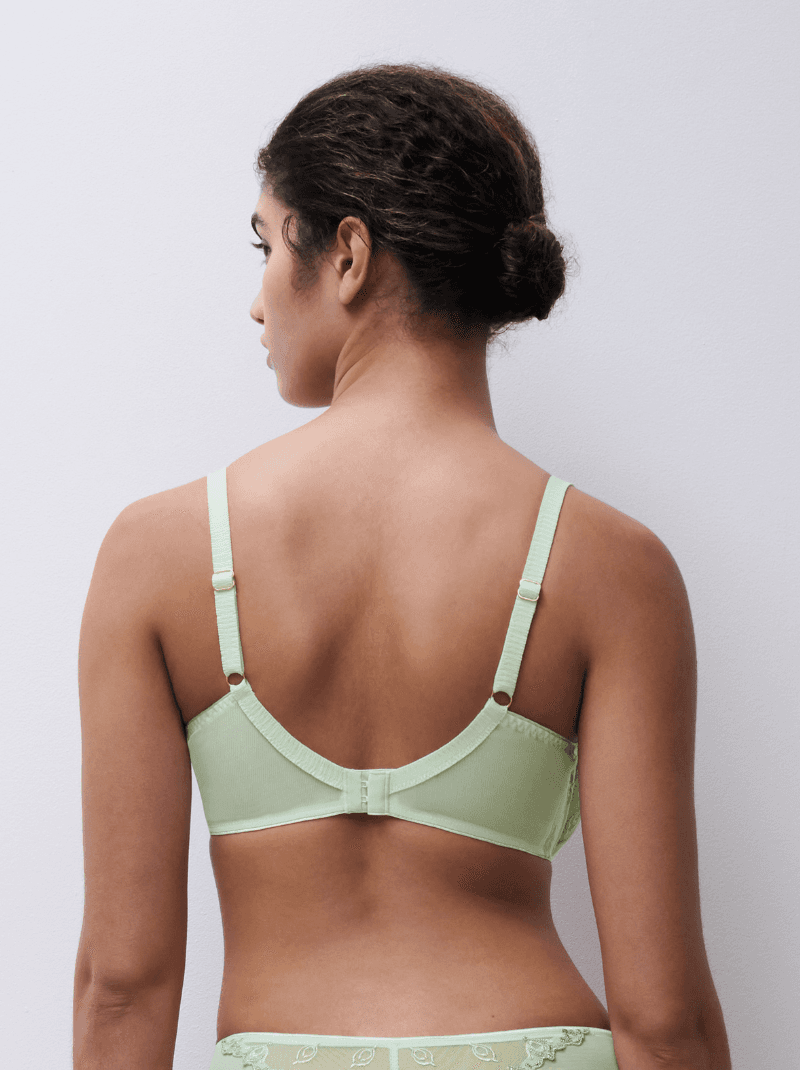 A person with curly hair in a bun wears a light green bra with adjustable straps, shown from the back against a plain white background.