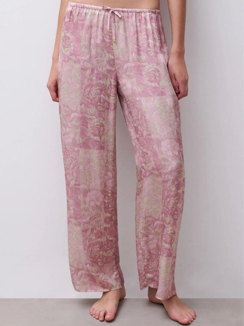 Person wearing loose-fitting, floral pink pajama pants with a drawstring, standing barefoot against a plain background.