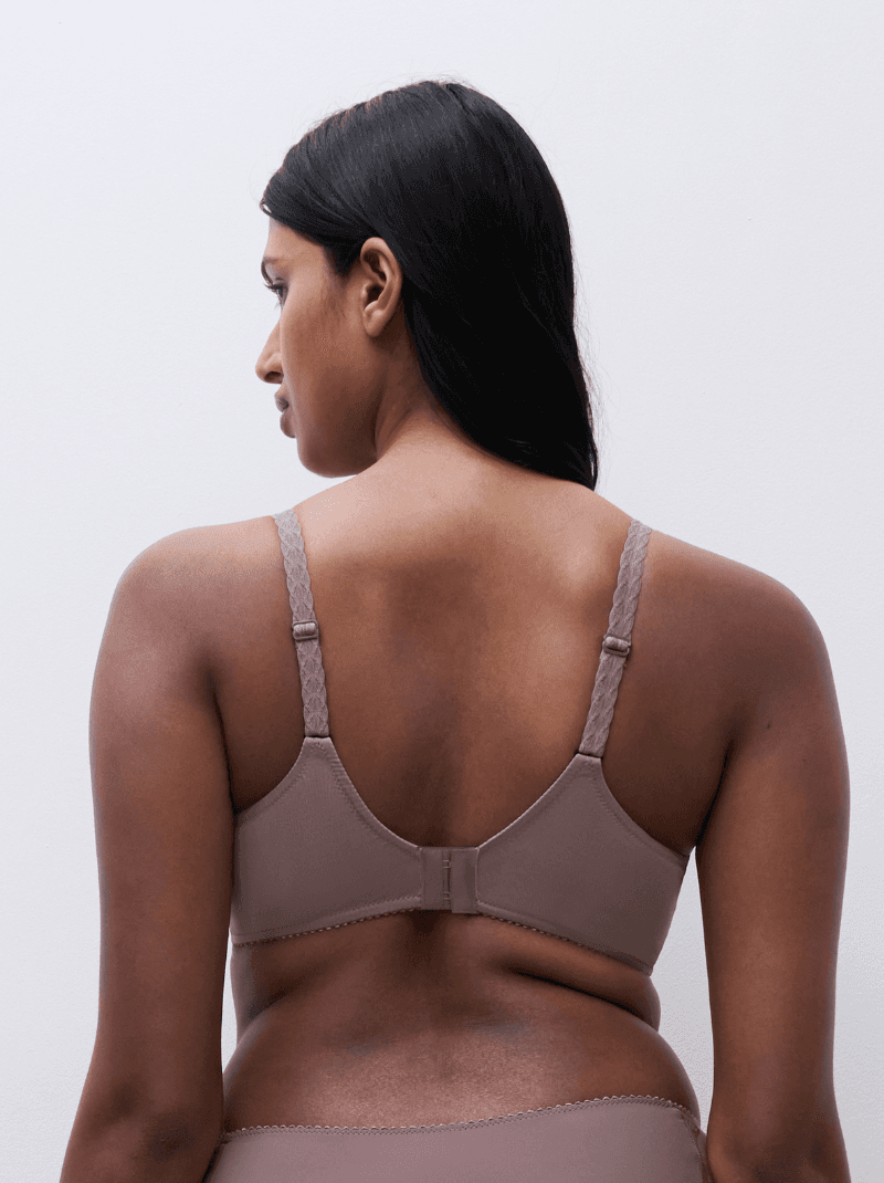 Rear view of a person with long hair wearing a beige bra, showing adjustable straps and hook closure, set against a plain background.