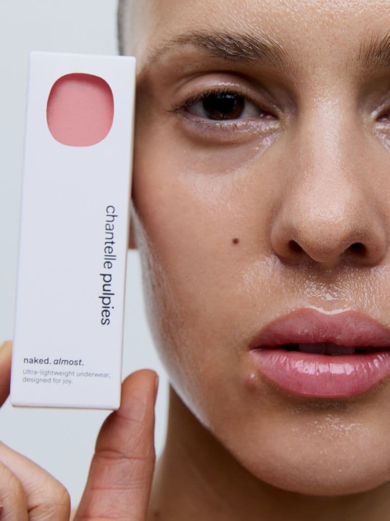 Close-up of a person with dewy skin holding a box labeled "chantelle pulpies," displaying a small pink product window.