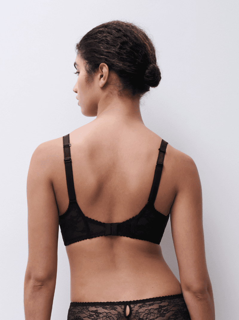 A woman with her back to the camera, wearing a black lace bra and panties, standing against a plain white background.