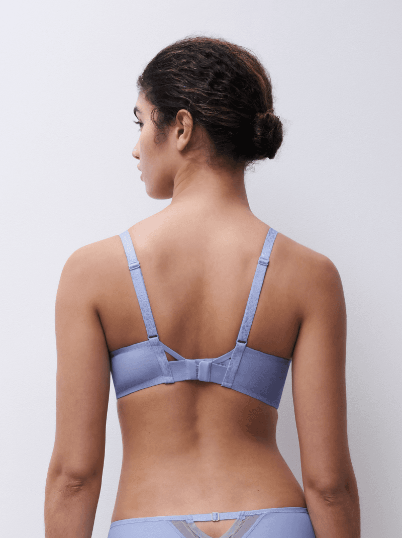 A woman with her hair in a bun is wearing a light blue bra, viewed from the back against a plain white background.