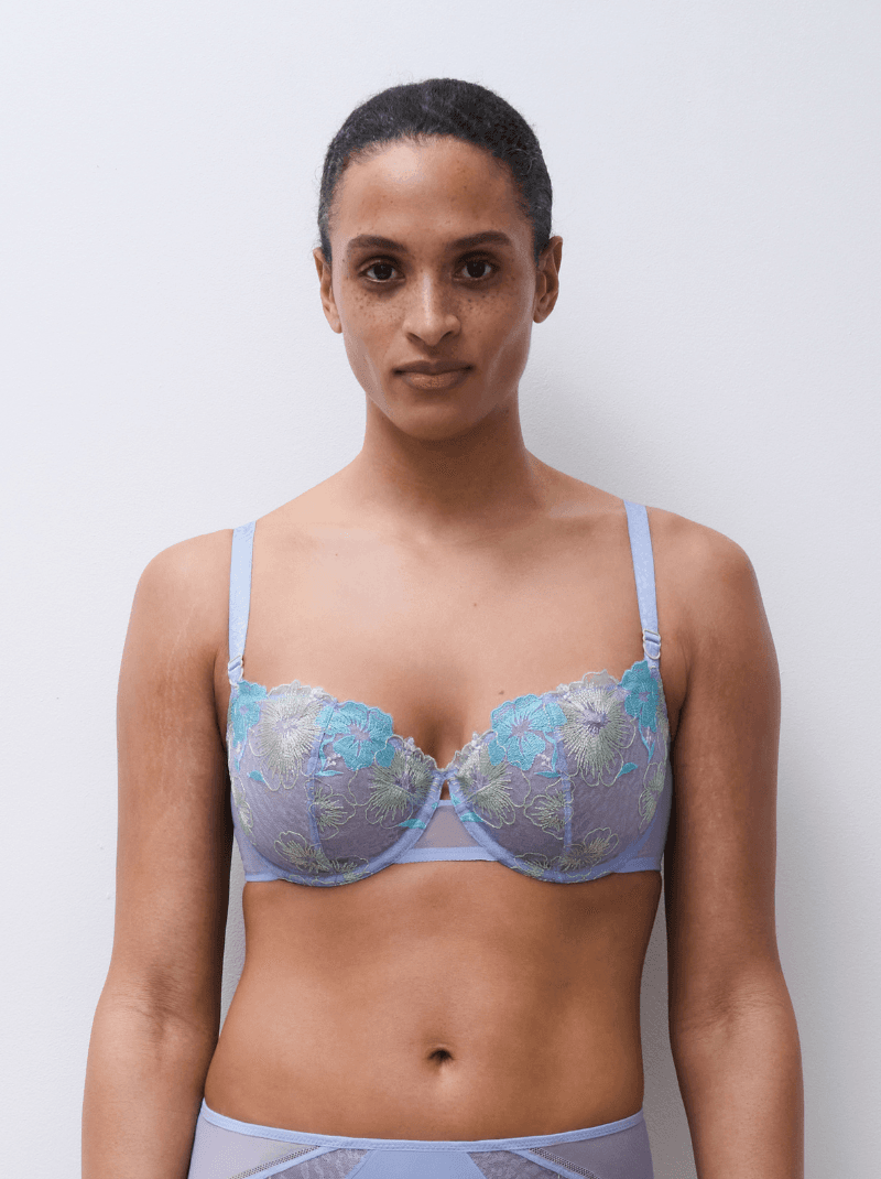 A person wearing a purple and turquoise lace bra, standing against a plain white background.