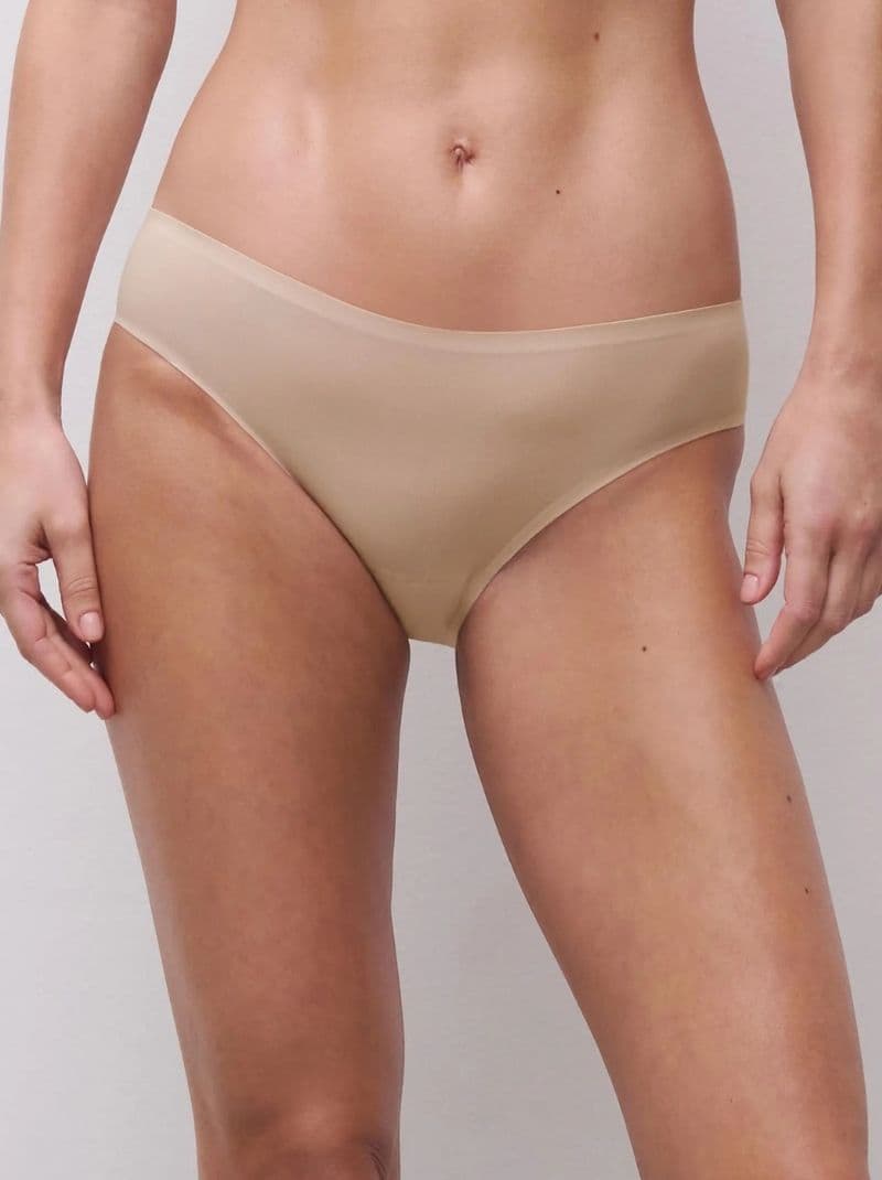 A person wearing seamless, golden beige colored underwear against a plain background, showing a front view from waist to mid-thigh.