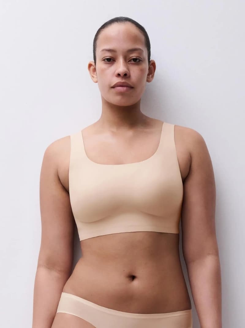 Person wearing a beige, seamless bra and underwear, standing against a light gray background.