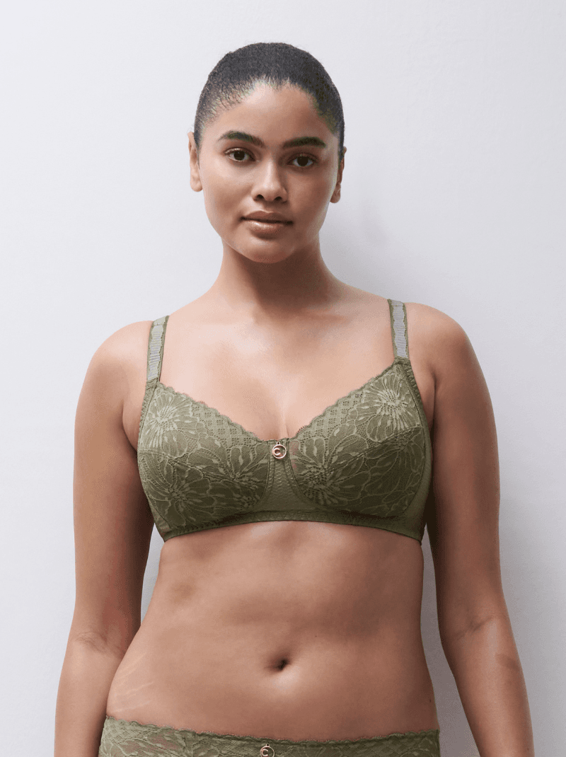 Person wearing a green lace bra and matching undergarments, standing against a plain background.