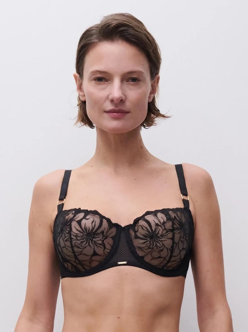 Person wearing a black lace bra with floral patterns, standing against a plain white background.