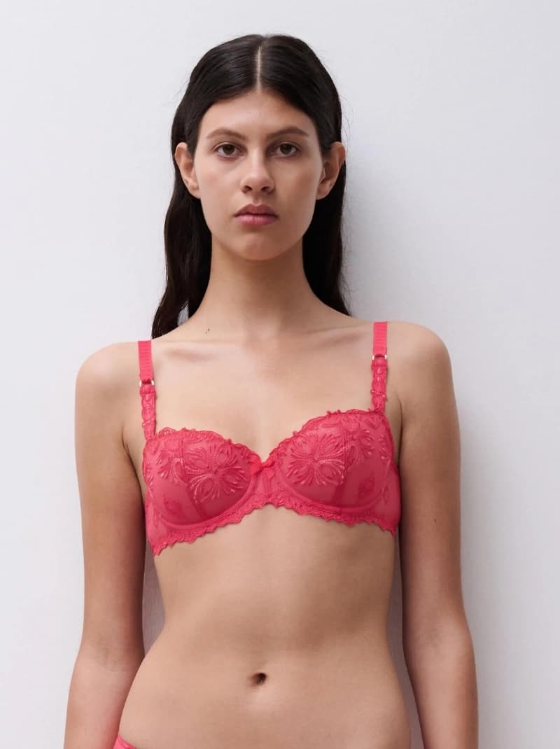 Woman wearing a pink floral lace bra, standing against a plain white background.