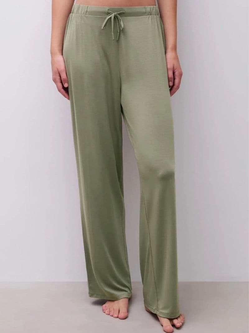 Person wearing loose-fitting, olive green pants, standing barefoot on a light floor.